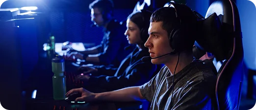 Competitieve gamers zitten op een rij tijdens een esports-toernooi, gefocust op monitoren onder blauwe podiumverlichting.