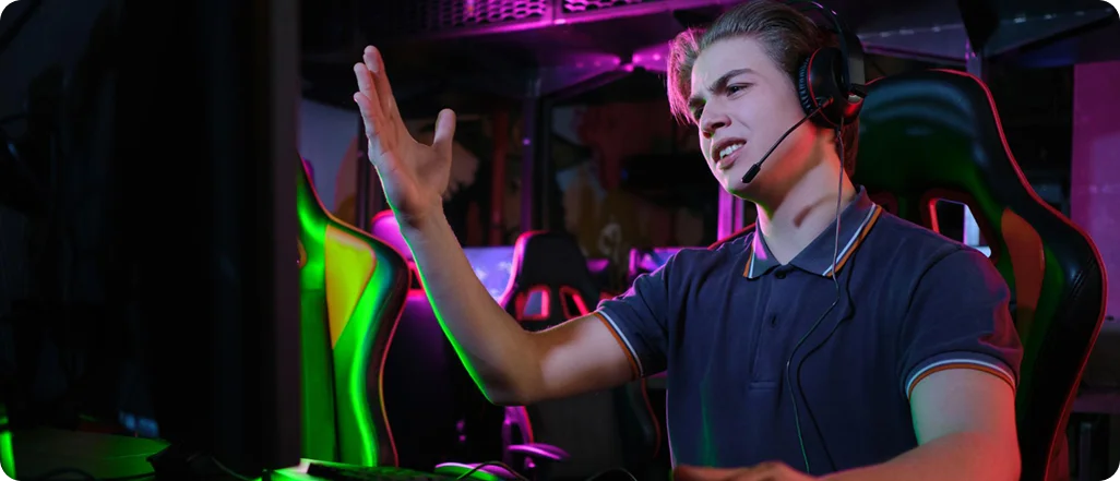 Jonge gamer reageert emotioneel tijdens een intense online wedstrijd terwijl hij streamt vanaf een kleurrijke RGB-gamingopstelling.