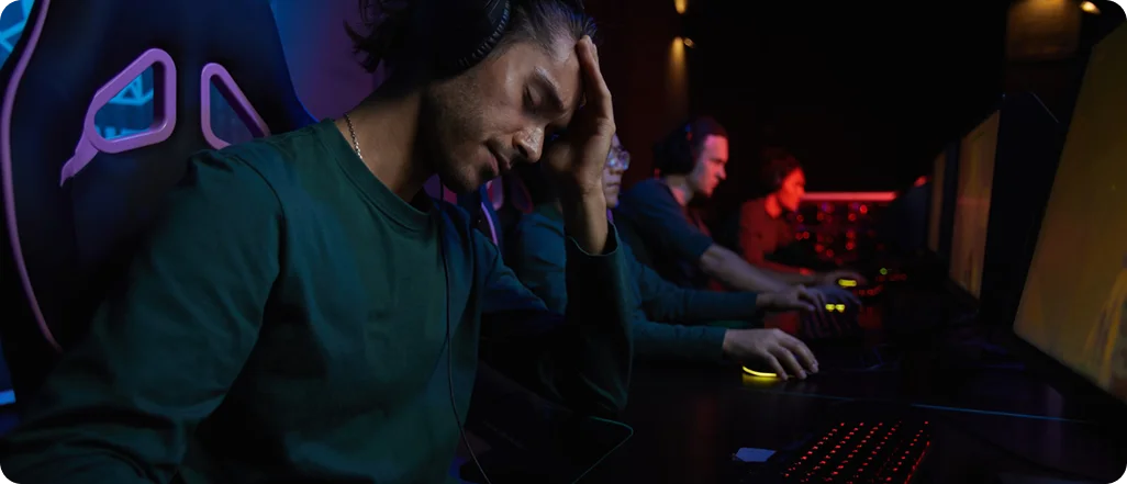 Gefrustreerde gamer houdt zijn hoofd vast na het verliezen van een wedstrijd tijdens een intense nachtelijke esports-sessie in een donkere gamingarena.